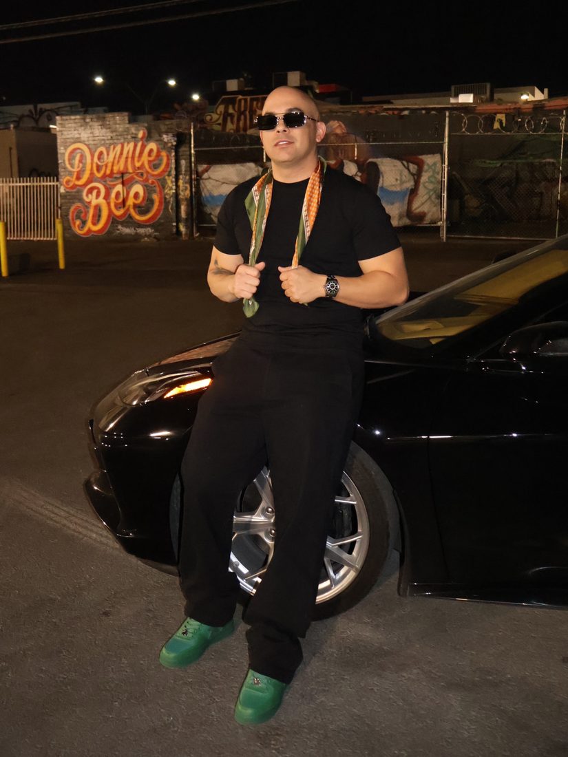 Total black con pañuelo y sneakers verdes junto a un deportivo negro